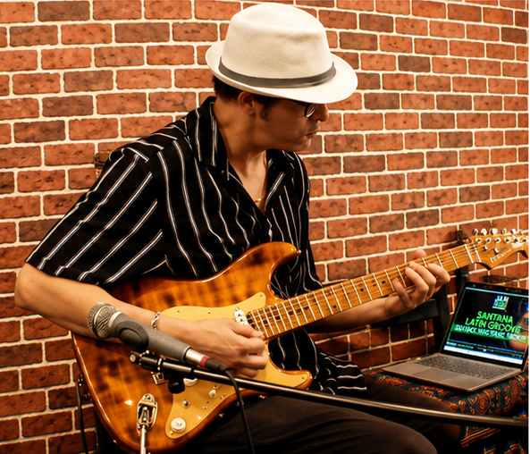 Houssam playing guitar in front of a brick wall